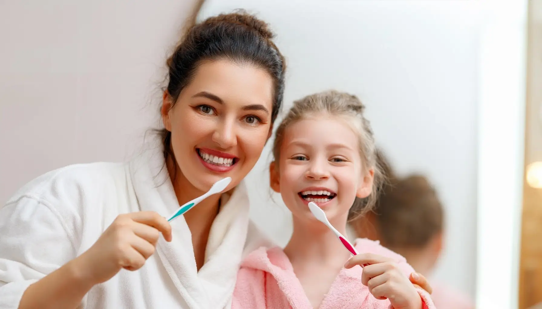 Illustration d'une mère et sa fille se brossant les dents ensemble dans la salle de bain, soulignant l'importance de l'hygiène bucco-dentaire quotidienne et de l'éducation à la santé dentaire dès l'enfance pour prévenir les caries interproximales.