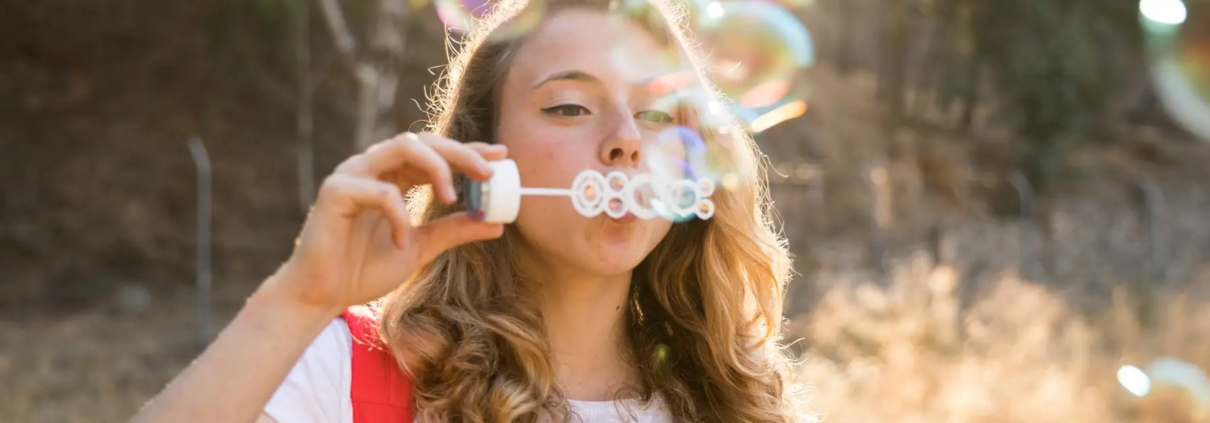 Jeune souriant en plein air, symbolisant une bonne santé dentaire et une alimentation saine, s'amusant avec des bulles rappelant la fraîcheur d'une routine de brossage efficace, en vojage,