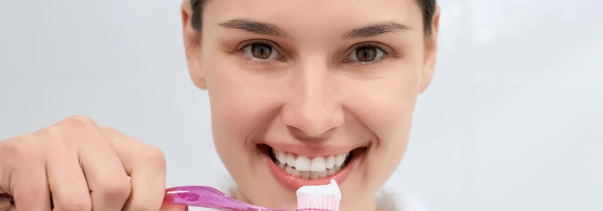 Femme tenant une brosse à dents rose avec du dentifrice dans la salle de bain.