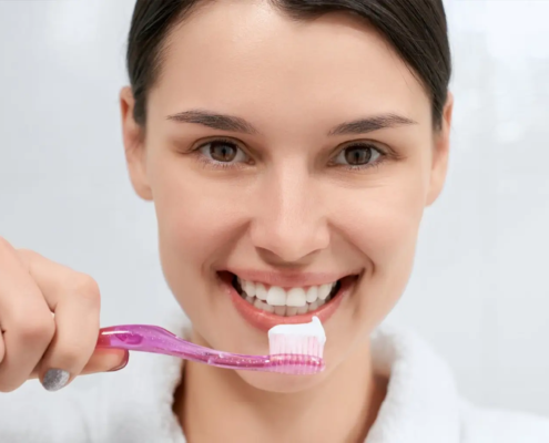 Femme tenant une brosse à dents rose avec du dentifrice dans la salle de bain.