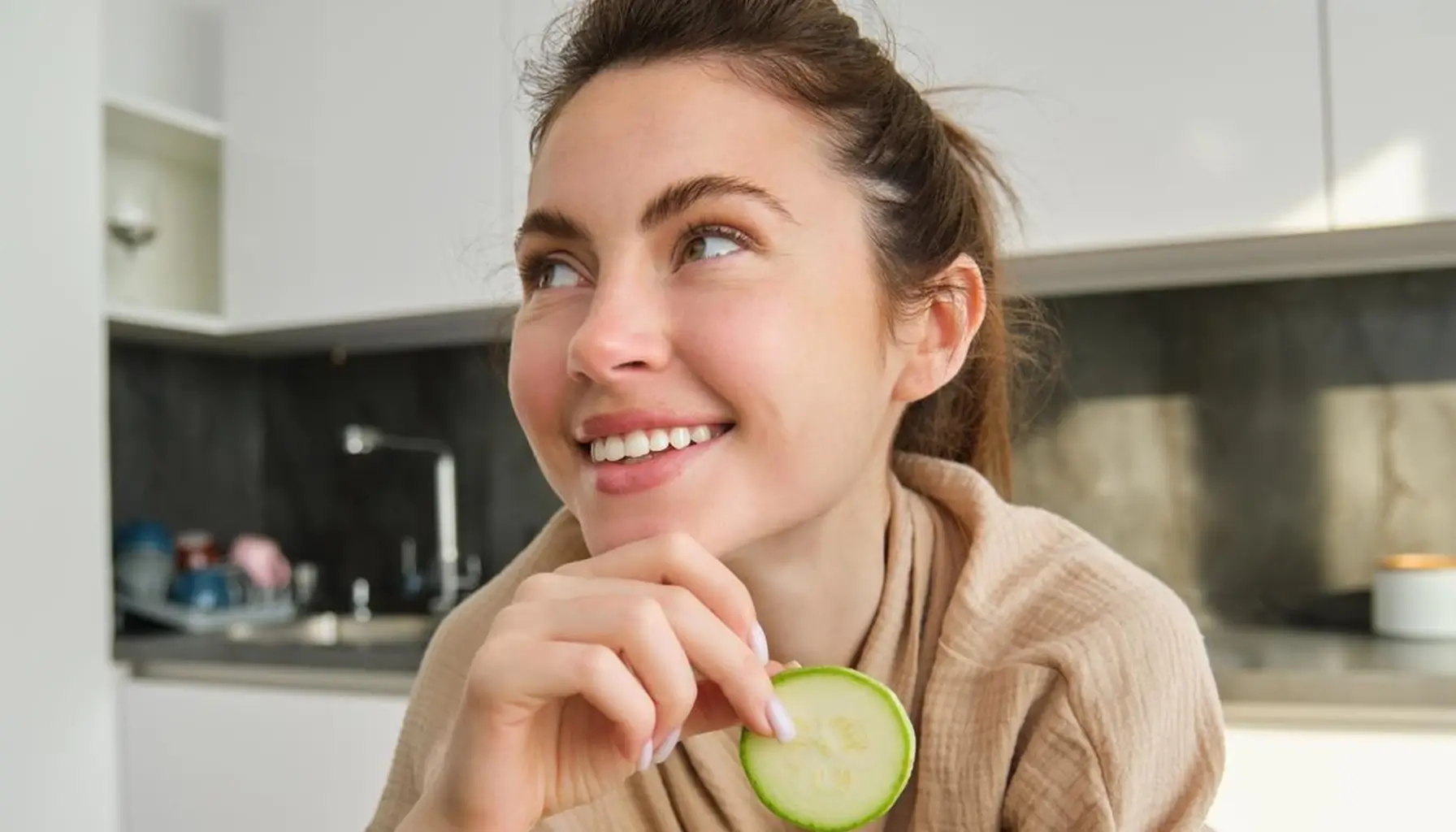 Une femme joyeuse, coupant des légumes dans sa cuisine, illustrant l'importance d'une alimentation santé dentaire et de la prévention dentaire.