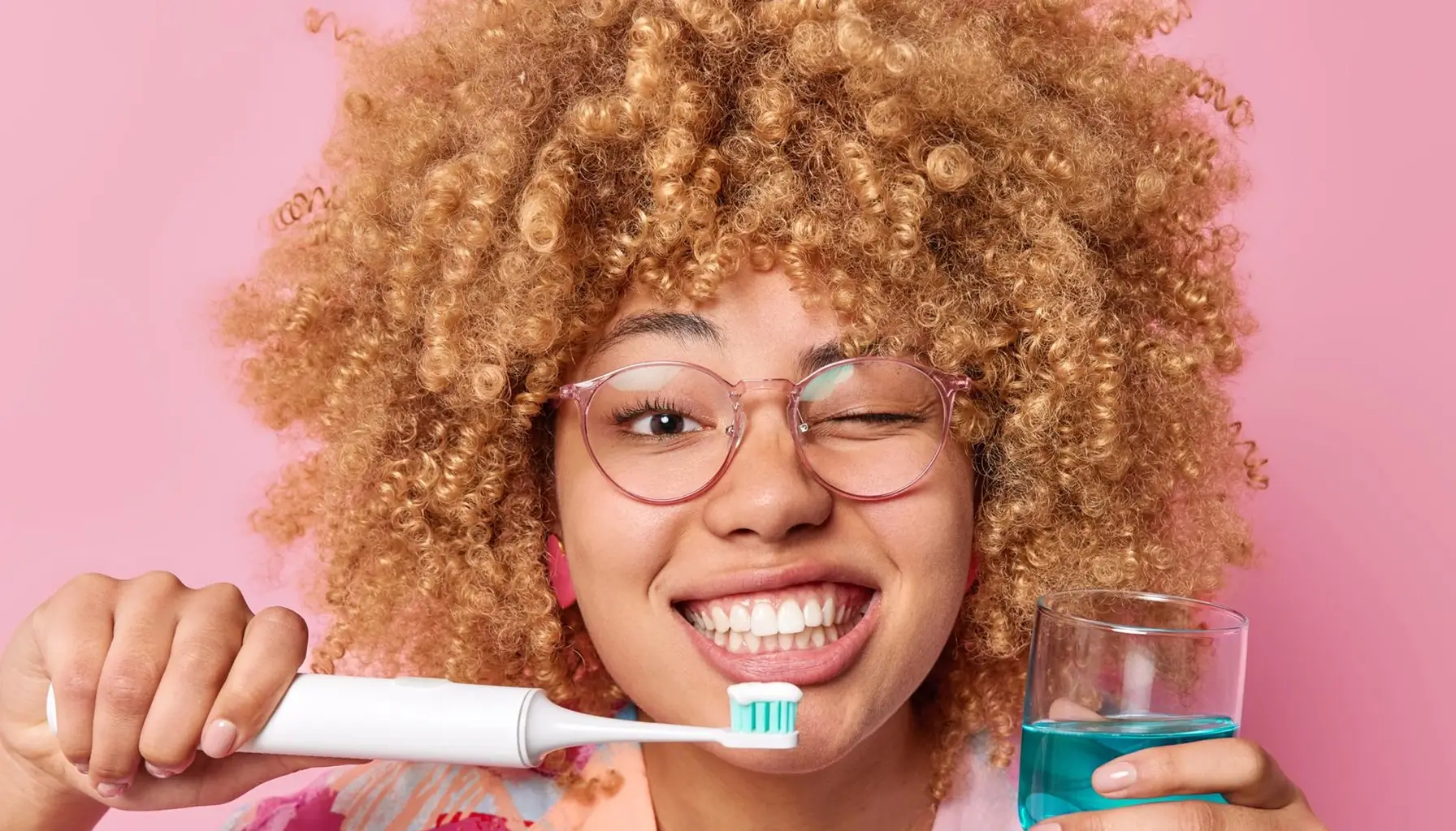 Femme souriante avec un bain de bouche et une brosse à dents électrique, illustrant une bonne hygiène bucco-dentaire pour prévenir les caries.