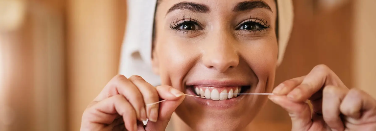 Femme se brossant les dents et utilisant du fil dentaire dans sa routine d'hygiène dentaire quotidienne.