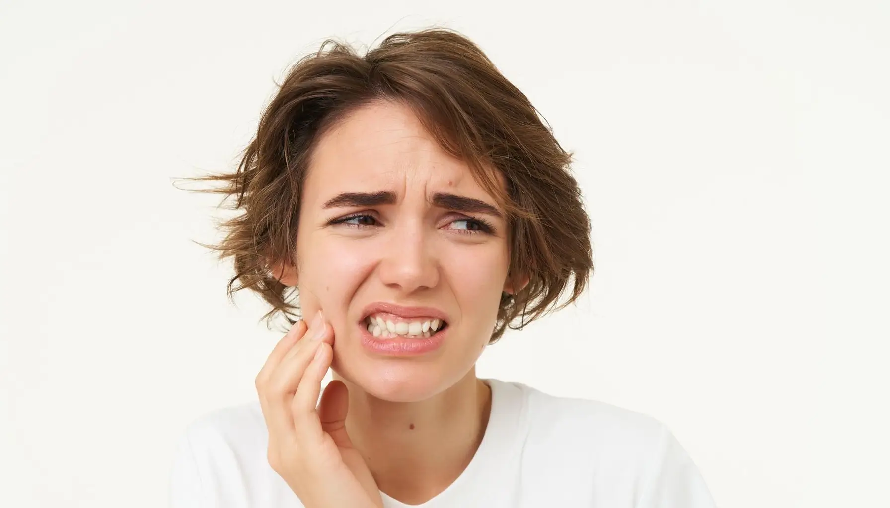 Femme touchant ses dents avec une expression douloureuse, illustrant les conséquences d'une mauvaise hygiène bucco-dentaire pouvant mener à la gingivite et à une mauvaise haleine