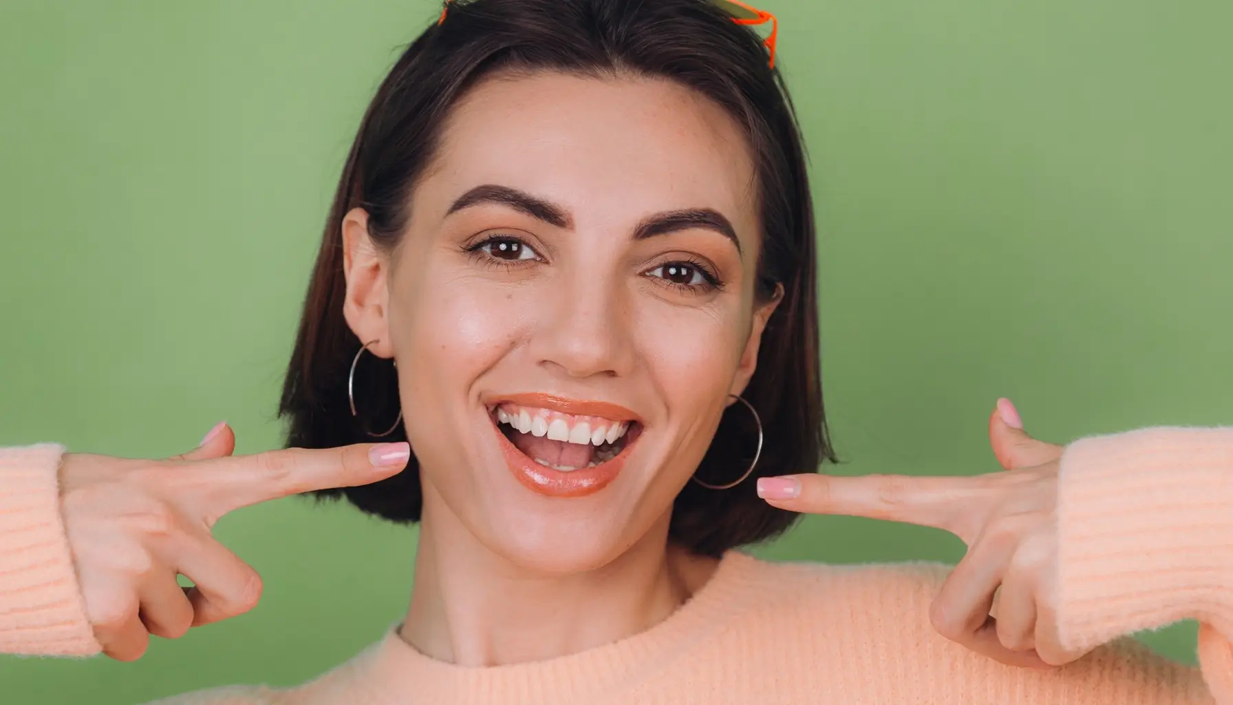 Femme souriante pointant ses dents blanches, mettant en avant l'importance de l'hygiène bucco-dentaire et la prévention des caries dentaires.