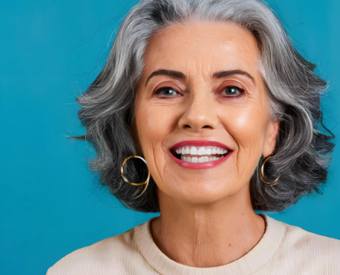 Femme senior affichant un sourire radieux grâce à des prothèses dentaires bien entretenues par des techniques de nettoyage efficaces et des produits adaptés, photographiée sur un fond bleu avec espace libre.