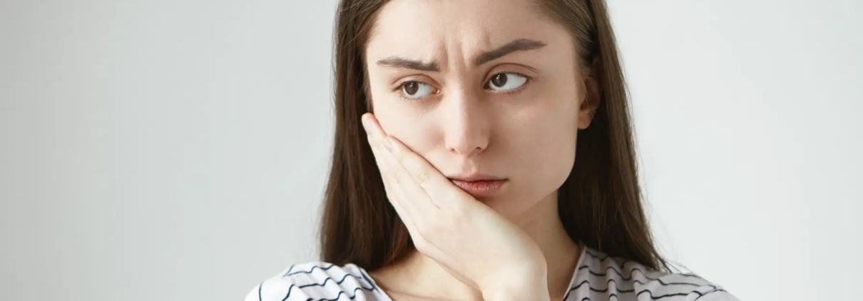 Jeune femme en détresse, victime de sensibilité dentaire, nécessitant un dentifrice spécial pour atténuer la douleur causée par les diverses causes de la sensibilité dentaire.