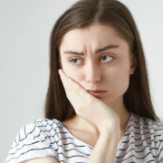 Jeune femme en détresse, victime de sensibilité dentaire, nécessitant un dentifrice spécial pour atténuer la douleur causée par les diverses causes de la sensibilité dentaire.