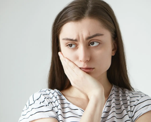 Jeune femme en détresse, victime de sensibilité dentaire, nécessitant un dentifrice spécial pour atténuer la douleur causée par les diverses causes de la sensibilité dentaire.