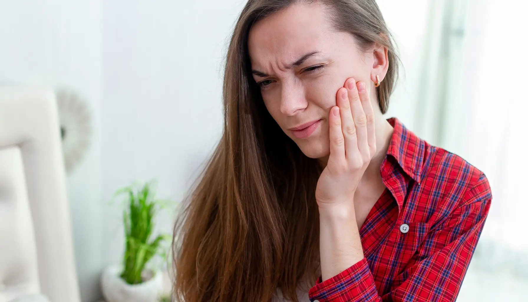 Femme expérimentant une sensibilité dentaire sévère, démontrant les conséquences des causes de la sensibilité dentaire et la nécessité d'un dentifrice spécial pour le traitement.