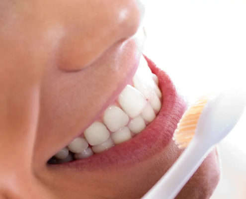 Gros plan d'une femme nettoyant ses dents, soulignant l'importance de l'hygiène dentaire, y compris le soin des ponts et couronnes.