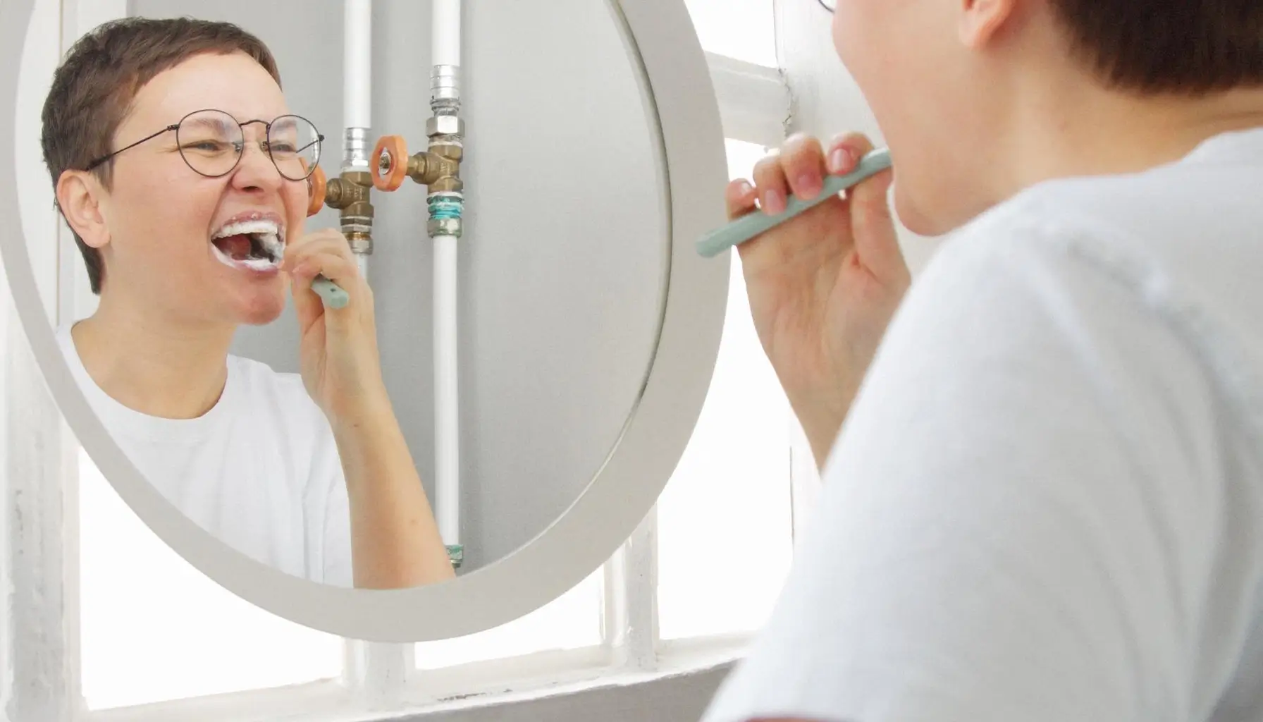 Femme se brossant les dents dans une salle de bain lumineuse, un rituel quotidien crucial pour maintenir une bonne hygiène dentaire. Éliminer la plaque dentaire et les bactéries buccales peut réduire le risque d'endocardite et d'autres maladies cardiaques, en complément d'une prophylaxie antibiotique si nécessaire.