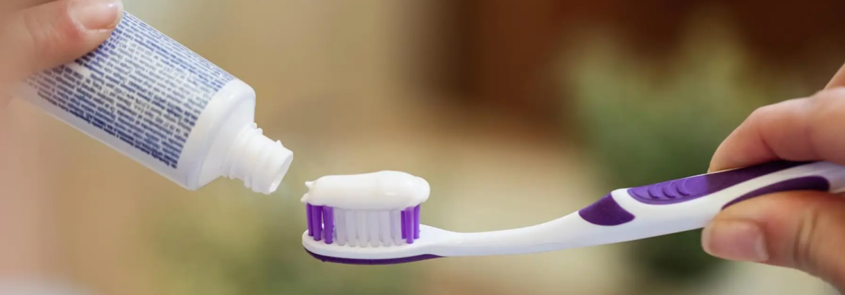 Femme mettant du dentifrice sur sa brosse à dents, un geste quotidien crucial pour l'hygiène bucco-dentaire. Les ingrédients des dentifrices, comme le fluor, aident à protéger les dents, tandis que les formules blanchissantes ou pour dents sensibles répondent à des besoins spécifiques. L'utilisation régulière de dentifrice, associée à des rince-bouches antibactériens, favorise une bonne santé dentaire.