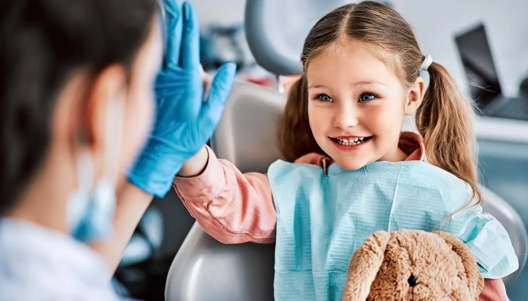 Enfant souriant tapant dans la main de l'infirmière dentaire, symbolisant une sensibilisation ludique à l'hygiène buccale.